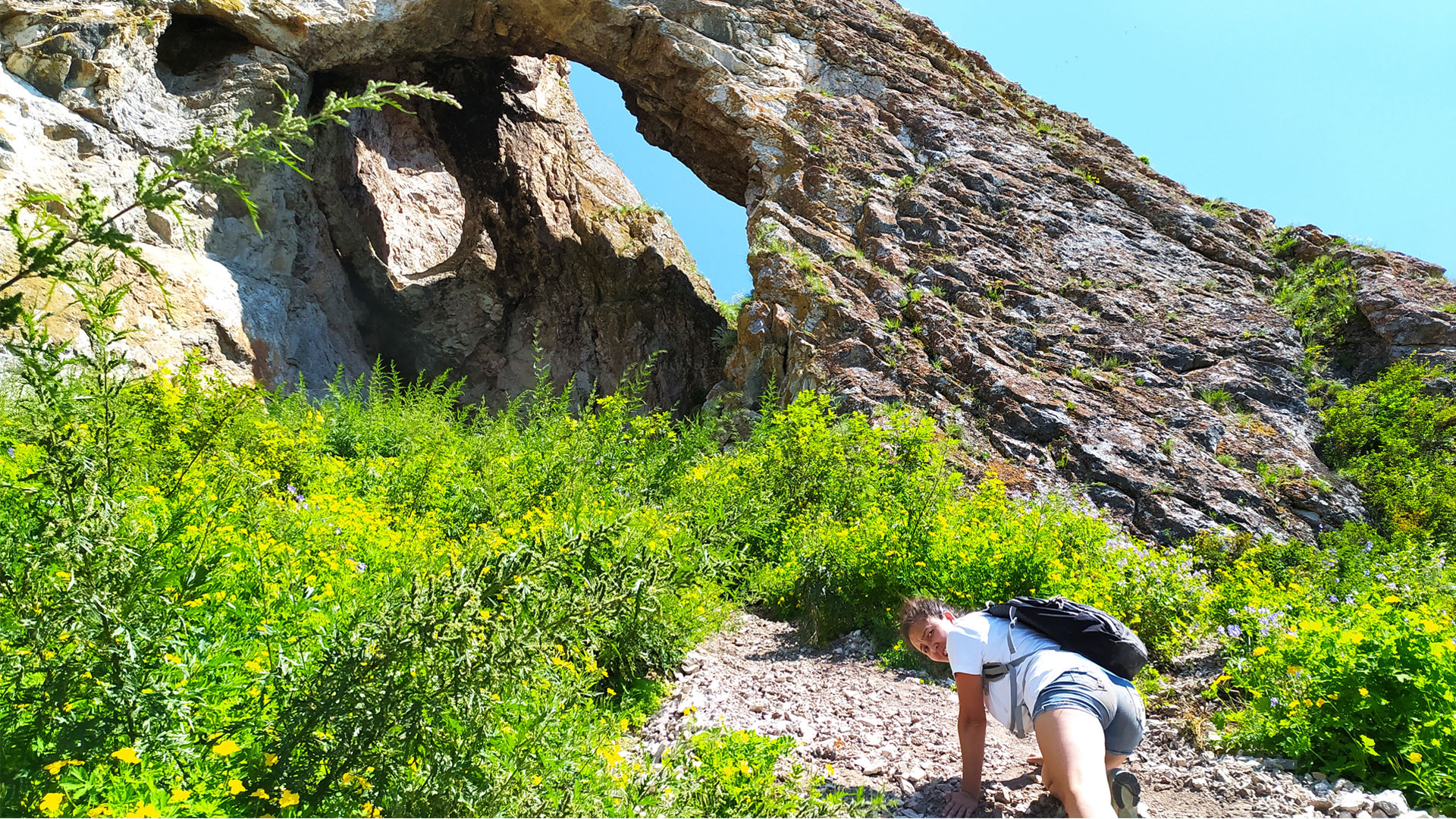 Девушка взбирается по крутому склону к арке в скале.