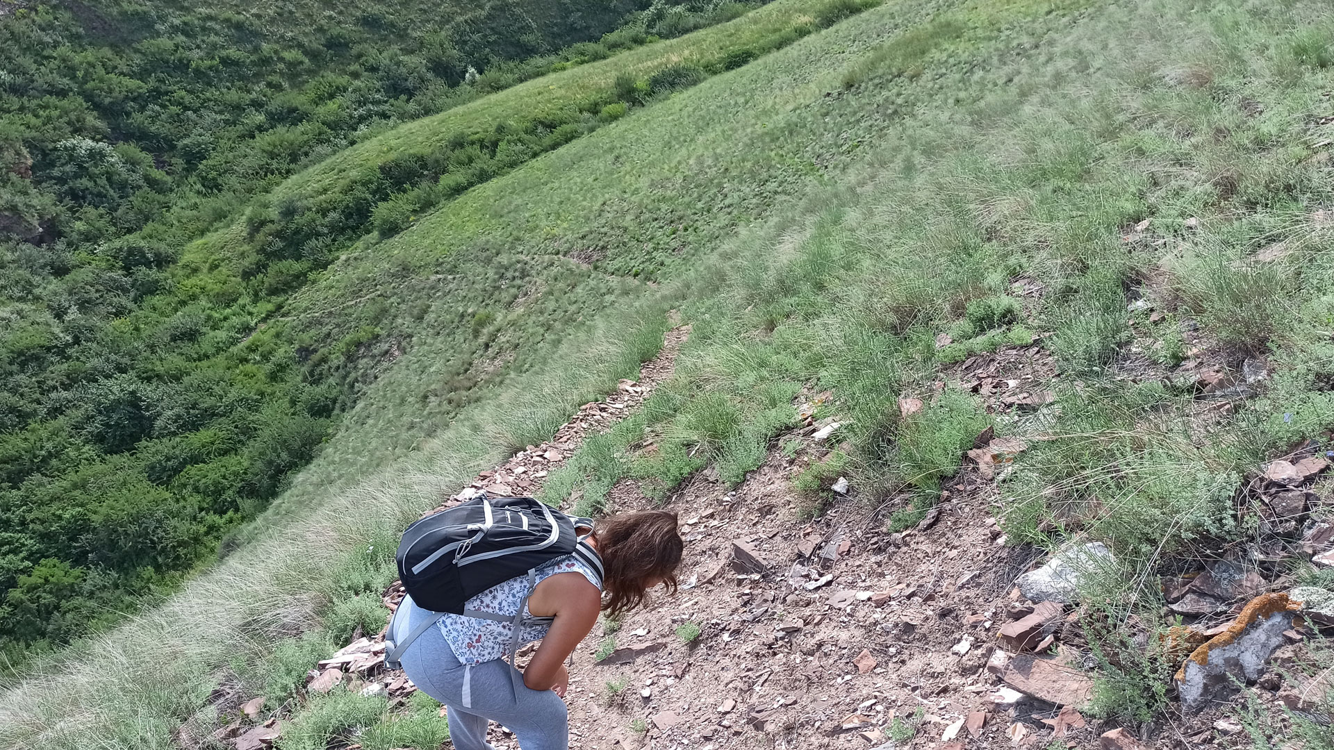 Девушка пригнувшись спускается с горы по узкой тропе.